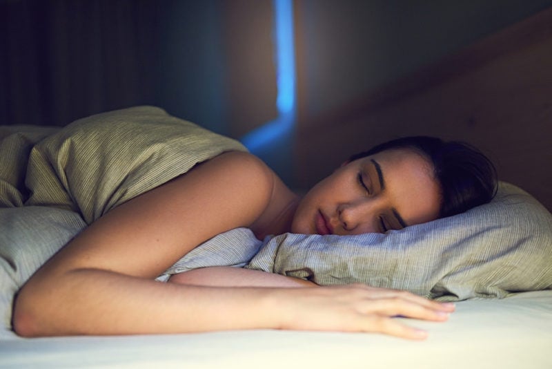 Shot of a young woman sound asleep in her bedroom ac sleeping benefits